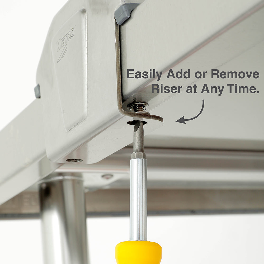 Metro TableWorx riser mounting bracket shown from beneath a stainless steel work table, illustrating easy attachment and removal using a screwdriver.