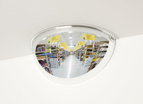 Half convex mirror in a store reflecting an aisle with shelves and signs.