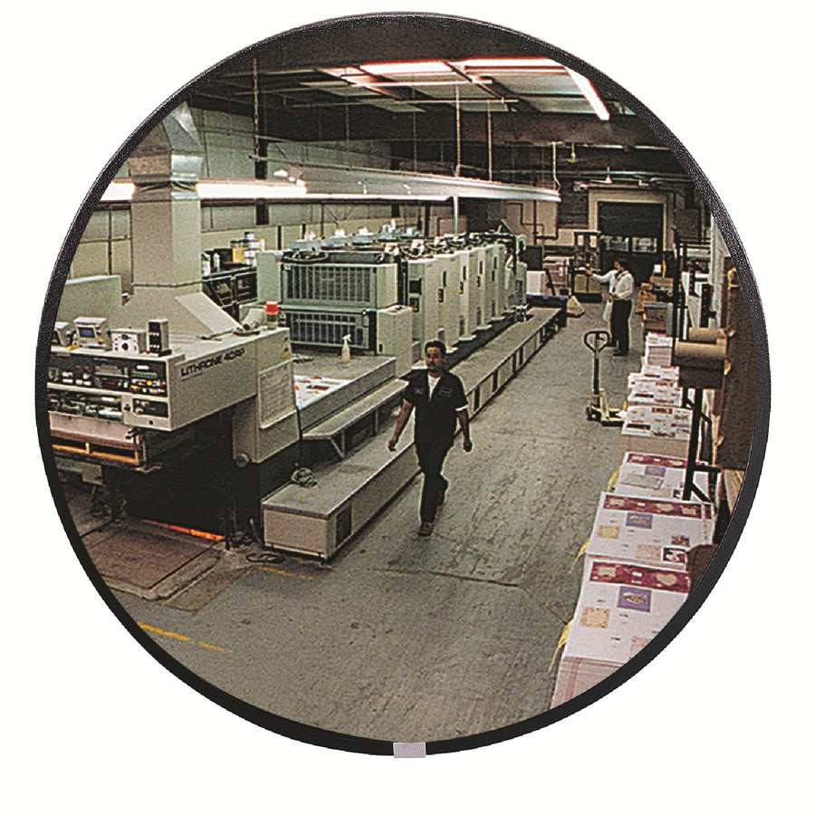 Person walking through a printing press room with large machines and stacks of paper, visible through round mirror.