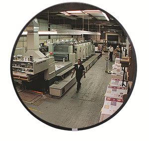 Person walking through a printing press room with large machines and stacks of paper, visible through round mirror.