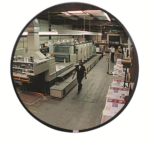 Person walking through a printing press room with large machines and stacks of paper, visible through round mirror.